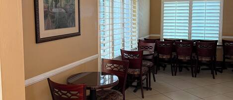 A dining area with a high ceiling, recessed lighting, and a large window with blinds.