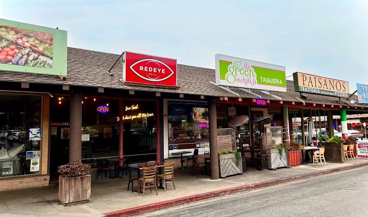 Eine Reihe von Restaurants mit Außenbestuhlung, darunter Schilder für 'REDEYE GRILL', 'the green enchilada' und 'PAISANOS TRATTORIA'.