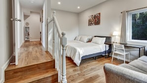 Quarto com cama, escrivaninha, cadeira e janela com vista para vegetação.