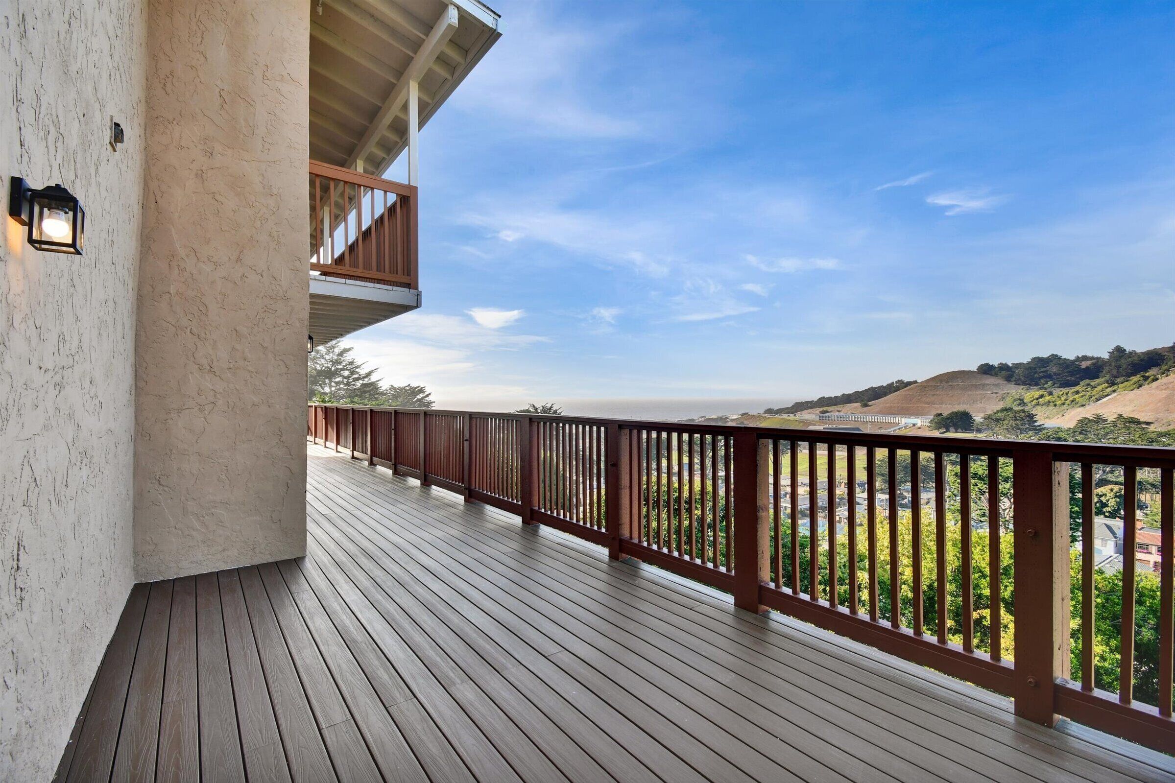 A wooden deck with a railing, a balcony, and a view of a hilly landscape.