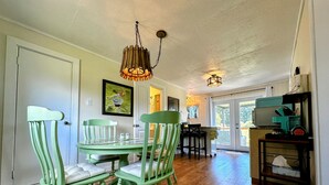 A dining area with a wooden table and four green chairs, a hanging light fixture, and a kitchen area with a stove and cabinets.