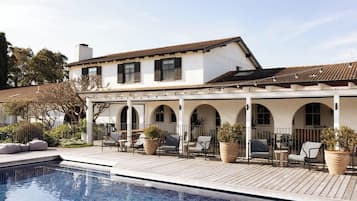 A poolside area with a covered patio, outdoor seating, and a swimming pool.