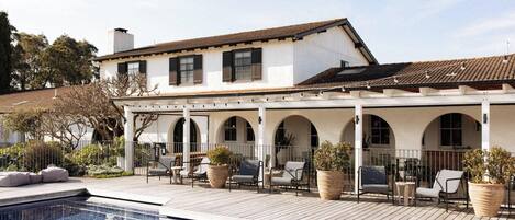 A poolside area with a covered patio, outdoor seating, and a swimming pool.