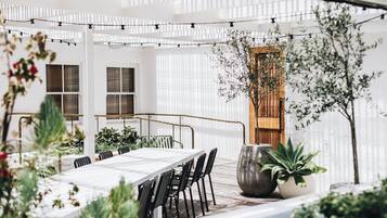 An outdoor patio area with a long dining table, chairs, and potted plants.