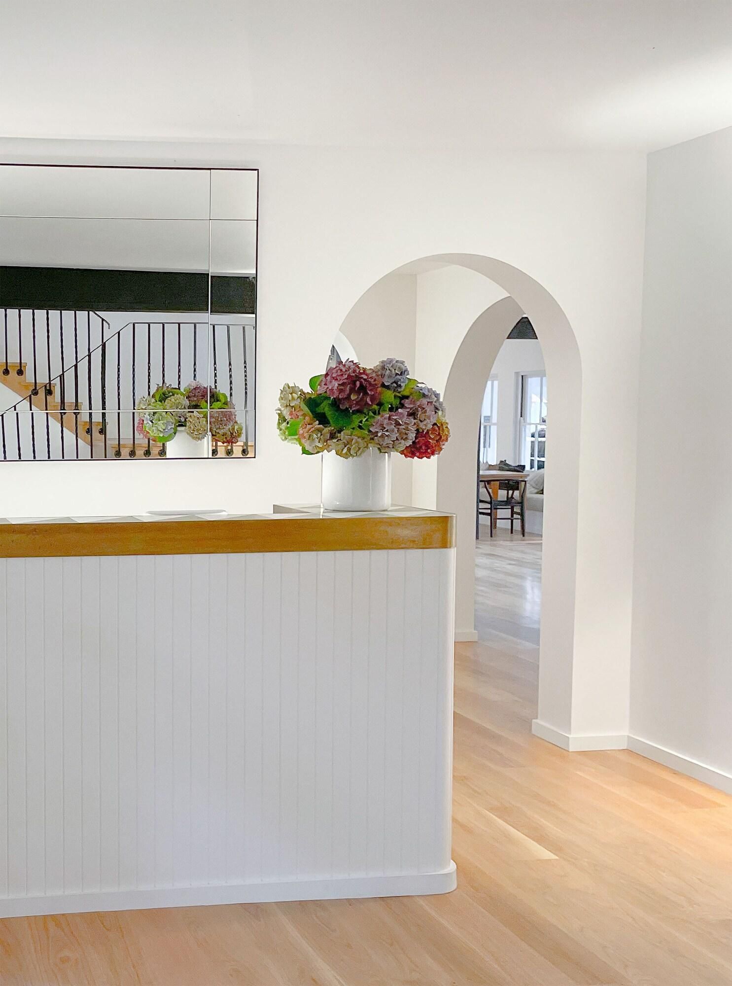 A reception area with a white reception desk, a mirror, and a floral arrangement.