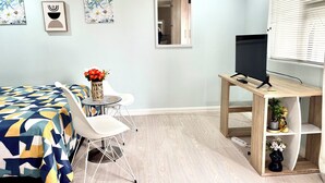 A bedroom with a bed, a small round table with chairs, a TV on a wooden stand, and wall art. - One Bedroom Bachelor A (Cape Town)