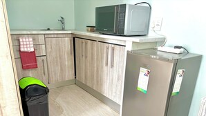 A compact kitchen with a microwave, a refrigerator, a sink, and a trash bin. - One Bedroom Bachelor A (Cape Town)