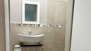 A bathroom with a white sink, a mirror, and beige tiles. - One Bedroom Bachelor A (Cape Town)