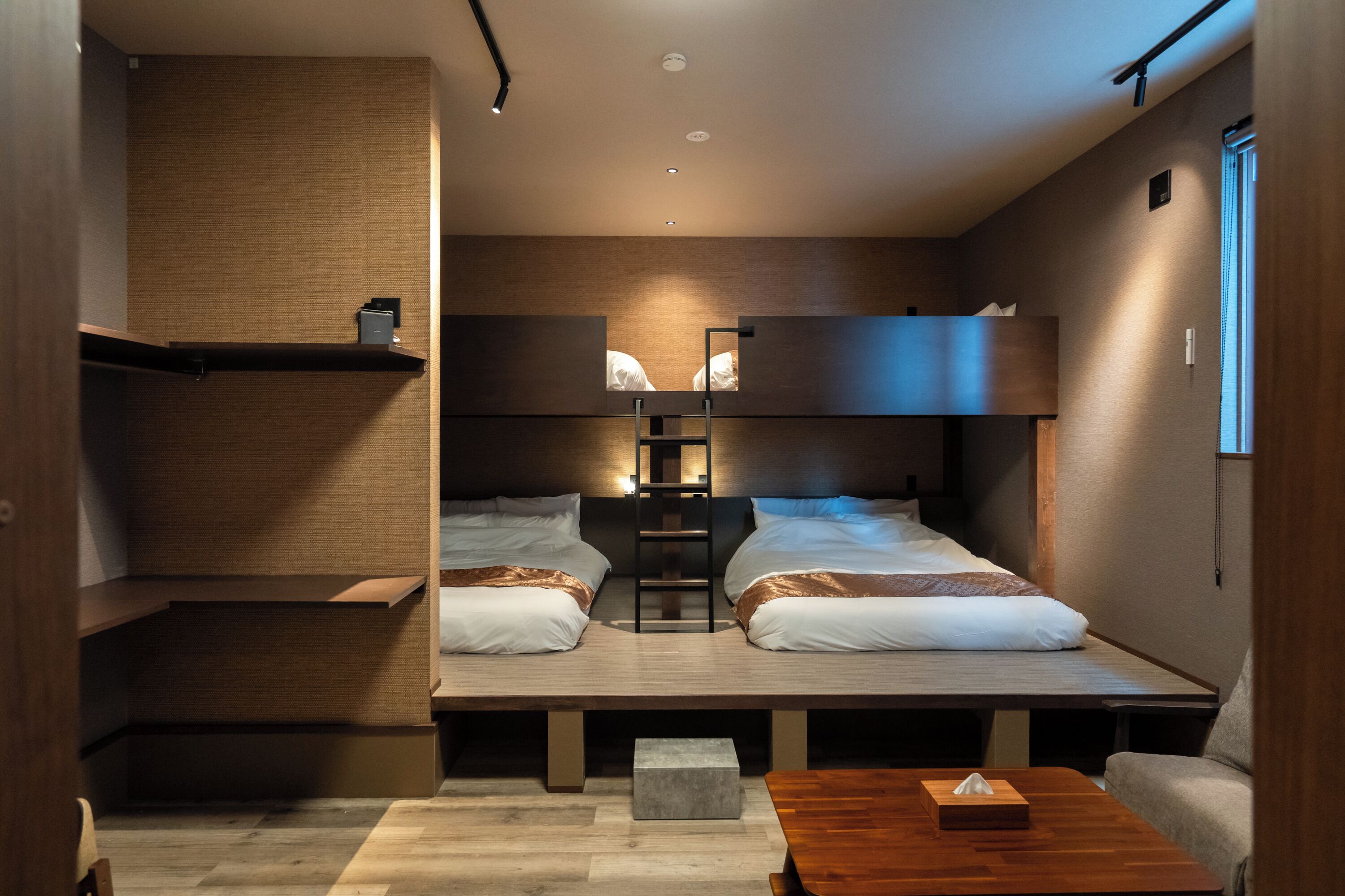 A modern hotel room with two beds, a wooden table, a bench, and a small seating area.