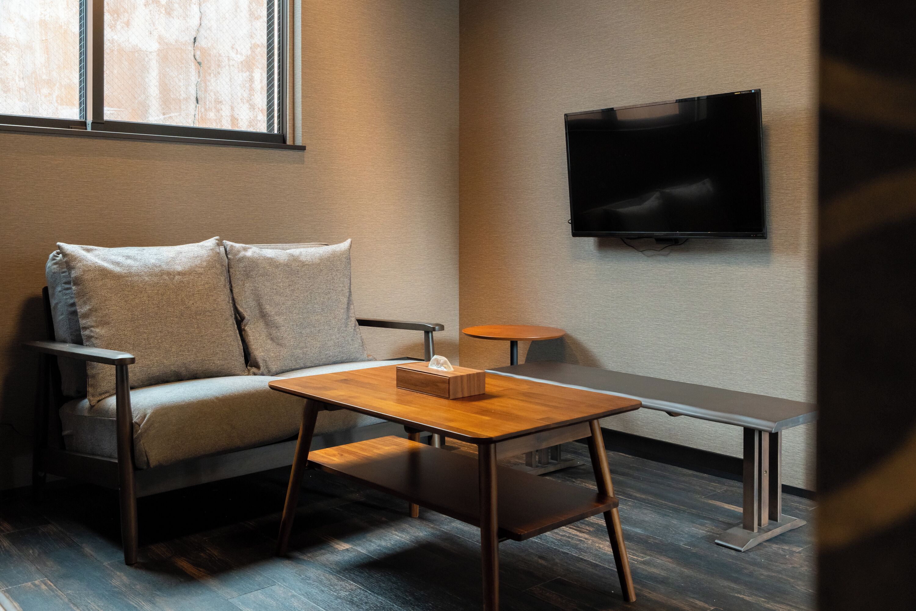 A modern room with a sofa, a wooden table, a bench, and a flat-screen TV mounted on the wall.