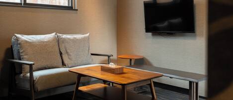 A modern room with a sofa, a wooden table, a bench, and a flat-screen TV mounted on the wall.