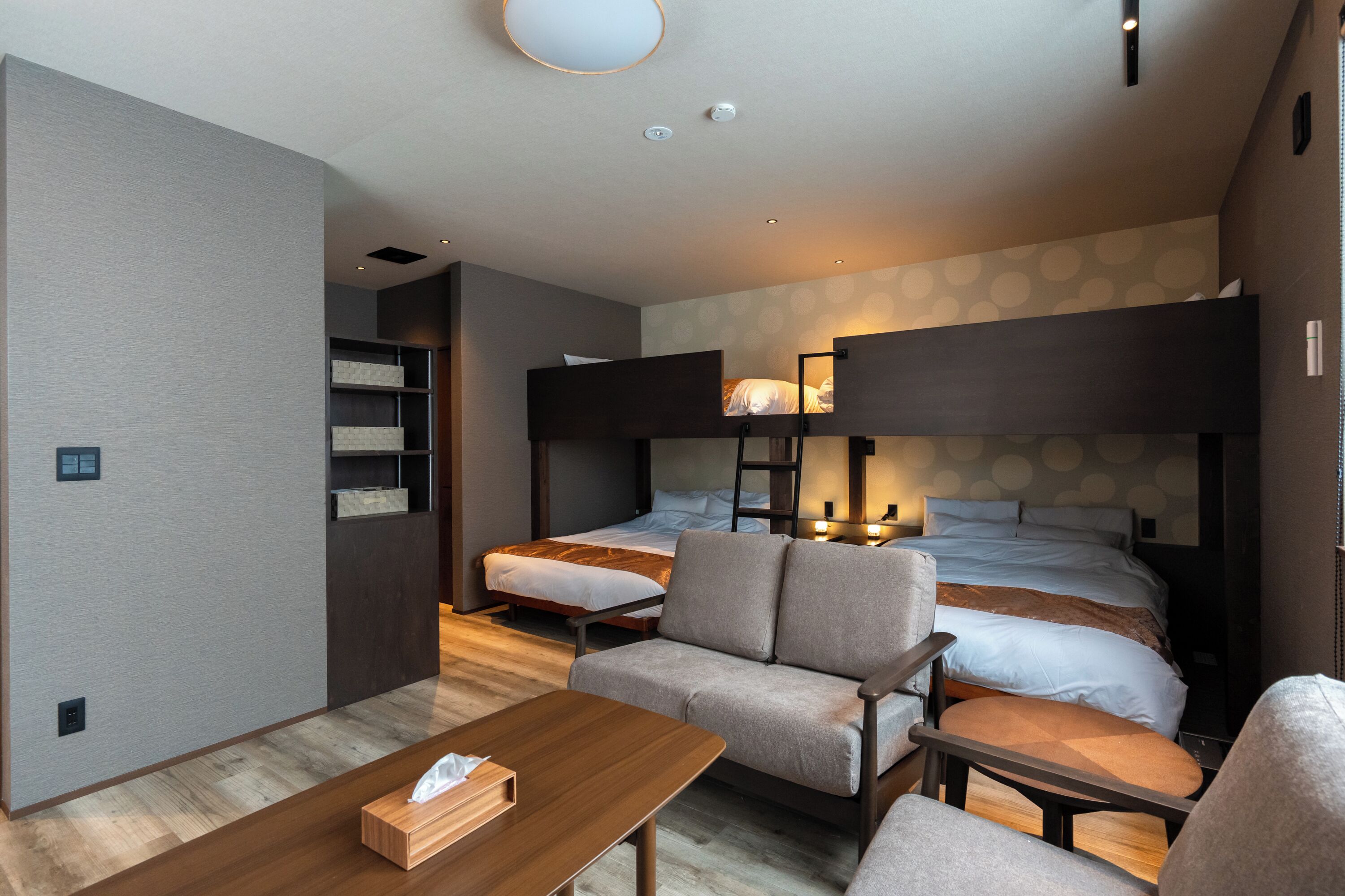 A modern hotel room with a sofa, two single beds, a desk, and a small table.