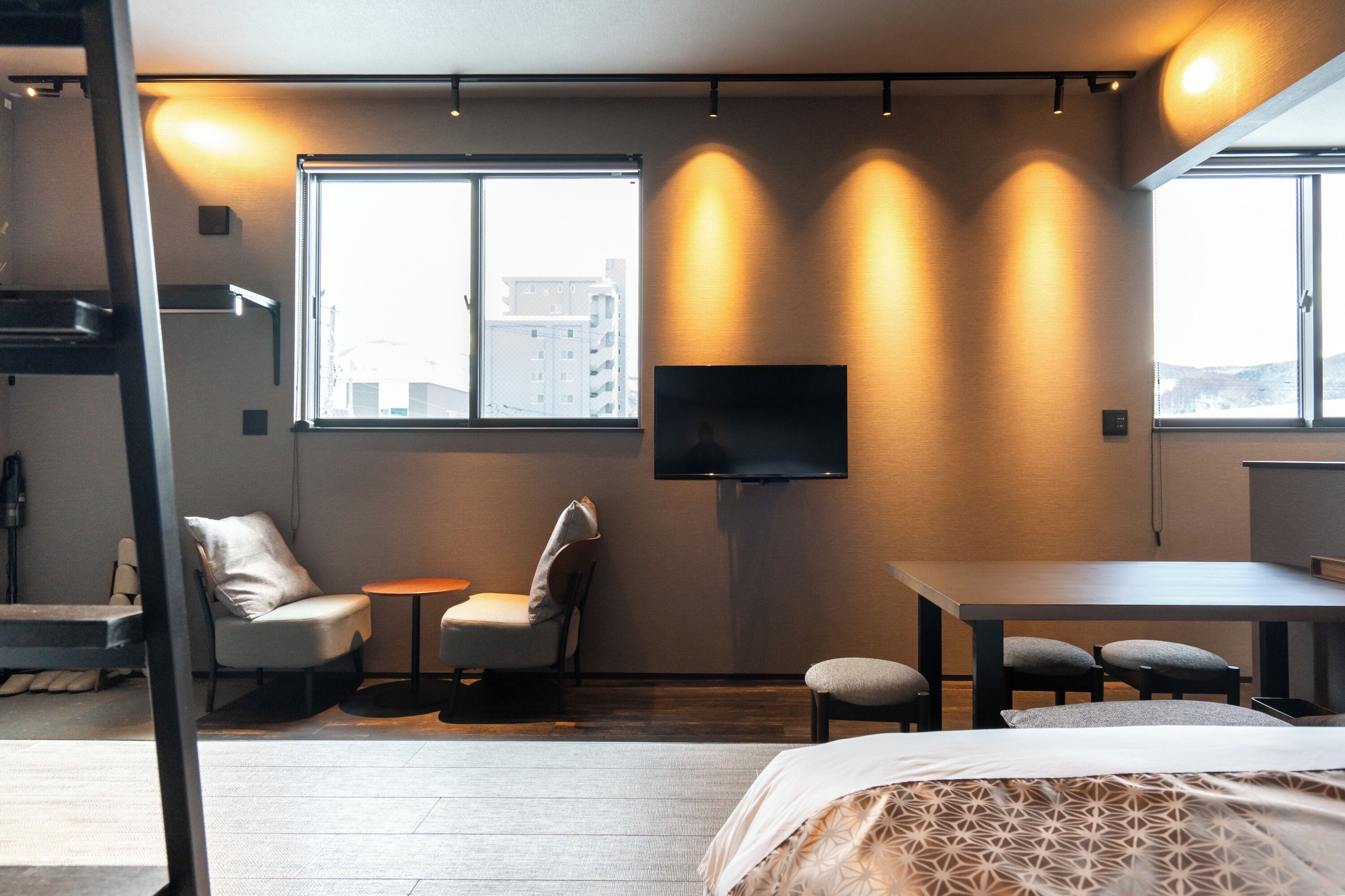 Una habitación de hotel moderna con una cama grande, un escritorio, dos sillas, una mesita y un televisor montado en la pared.