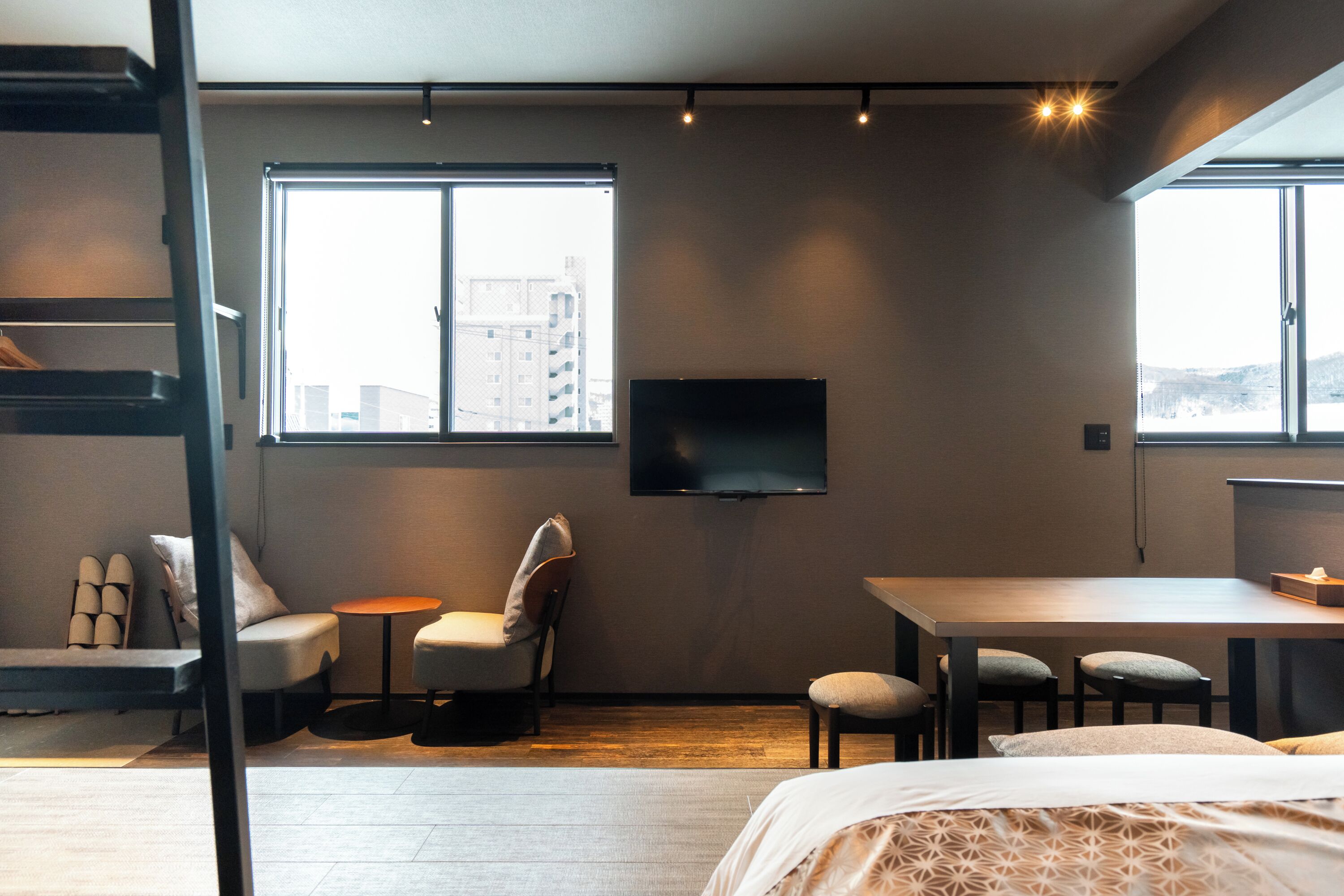 A modern hotel room with a bed, a desk, a chair, a small table, and a TV mounted on the wall.