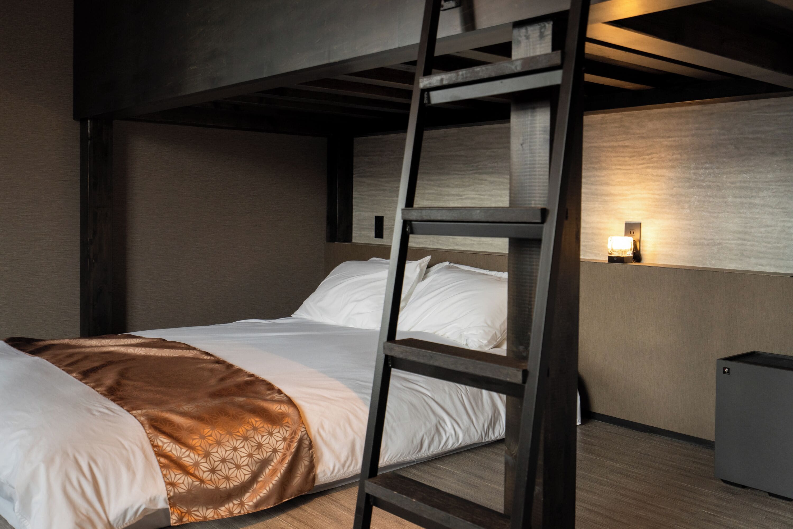 A bunk bed with a ladder, a bedside table, and a wall-mounted light.