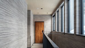 Un pasillo moderno con puerta de madera, ventanas amplias y barandilla metálica.