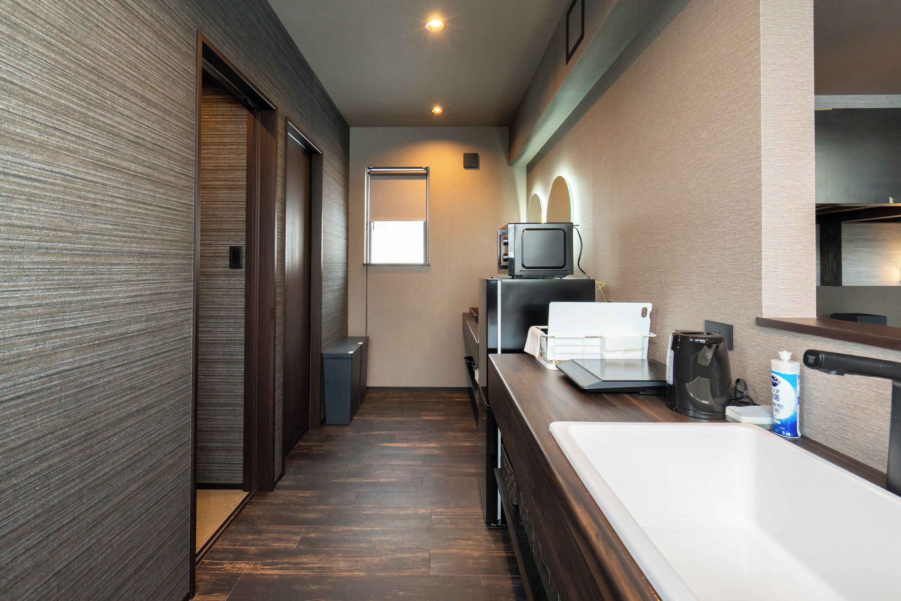 Een moderne hotelkamer met een houten vloer, een kleine kitchenette, een televisie en een raam.