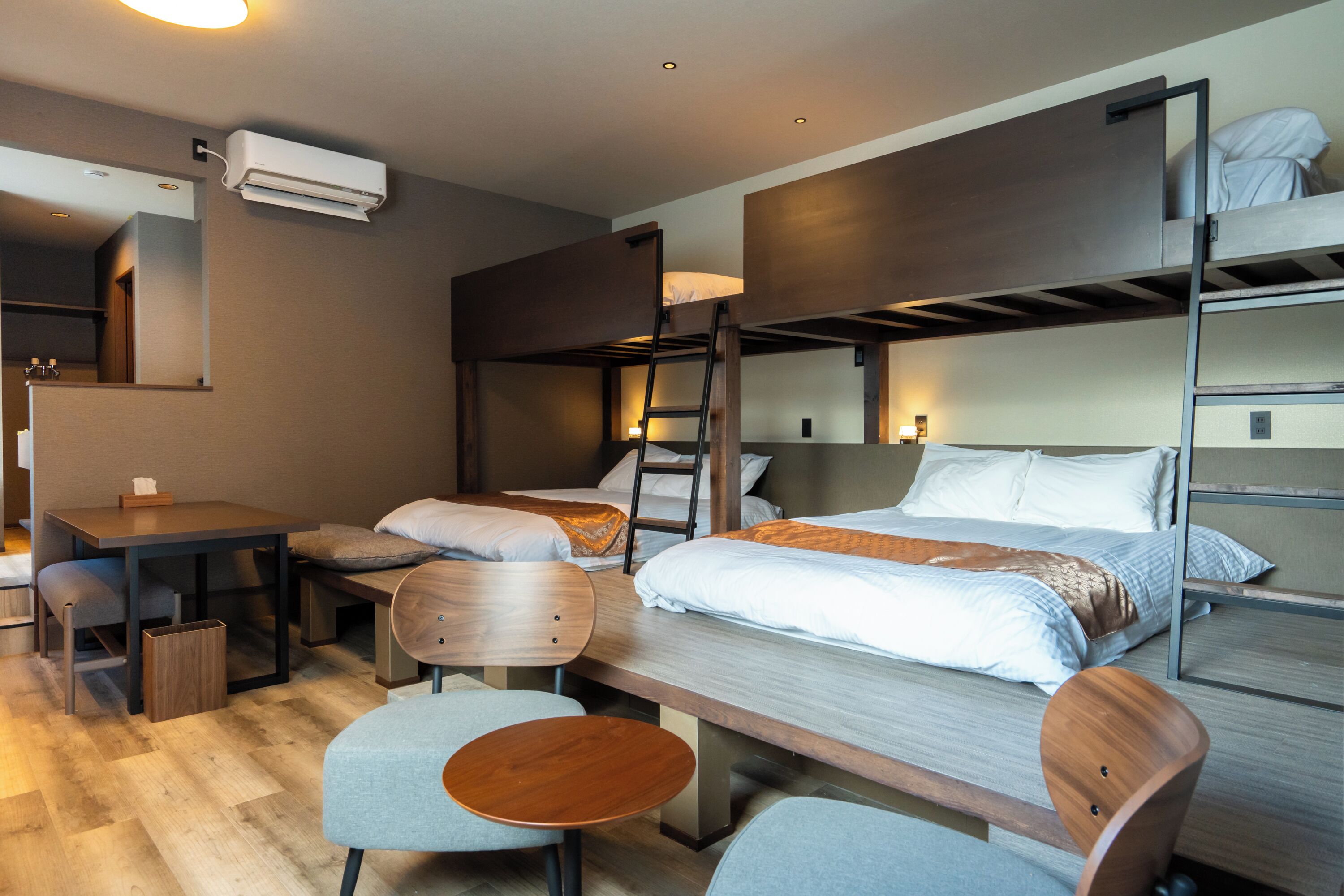 A compact hotel room with bunk beds, a desk, chairs, and a small table.