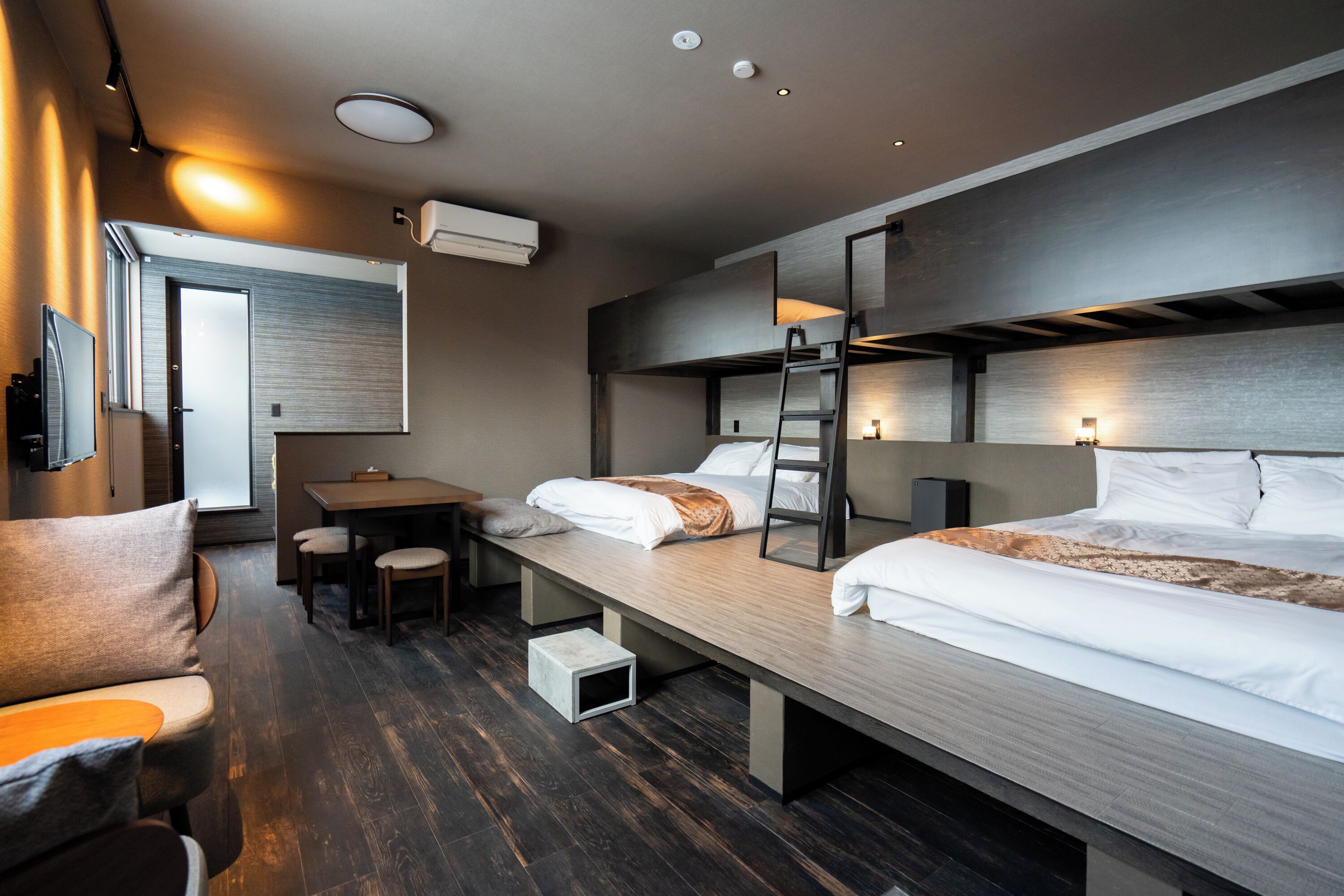 A modern hotel room with a bunk bed, a desk, and a seating area.