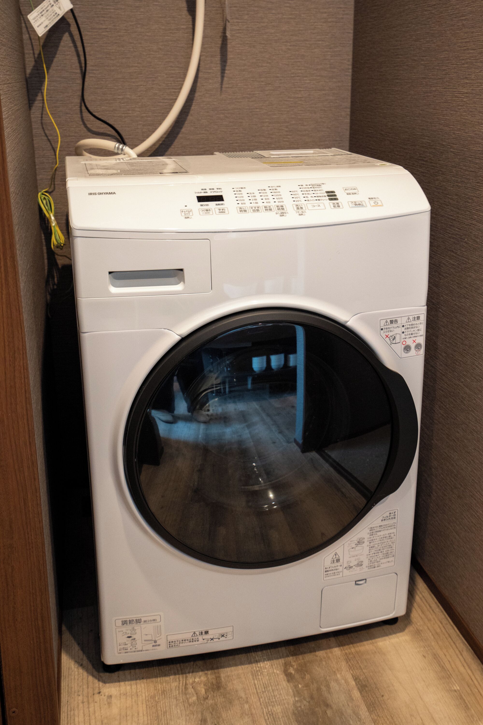 A front-loading washing machine with a control panel, a power cord, and a safety warning label.