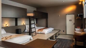 A hotel room with bunk beds, a desk, and a chair. There is a door, a coat hanger, and a small table.