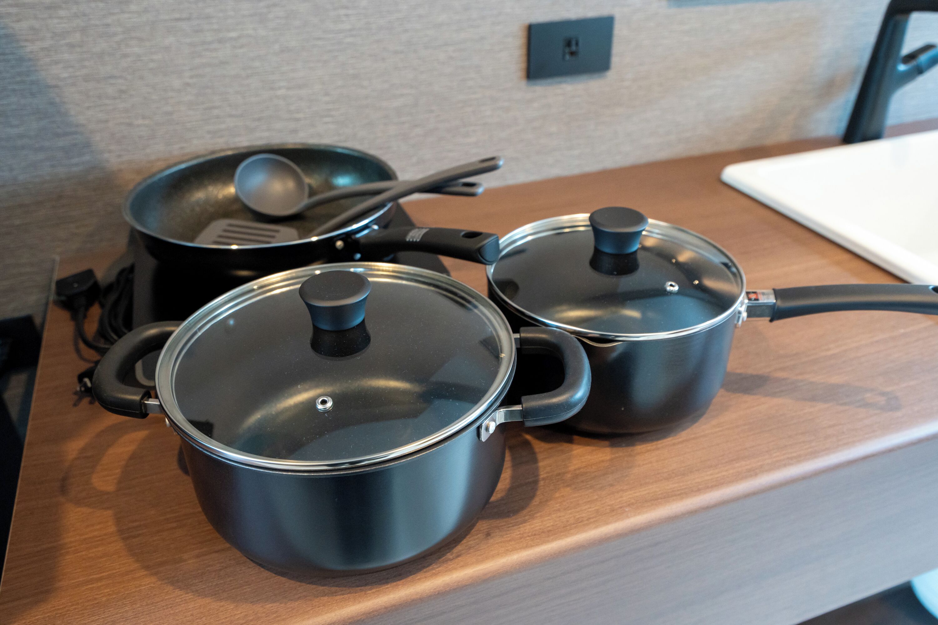 Three stainless steel pots with lids on a wooden countertop.