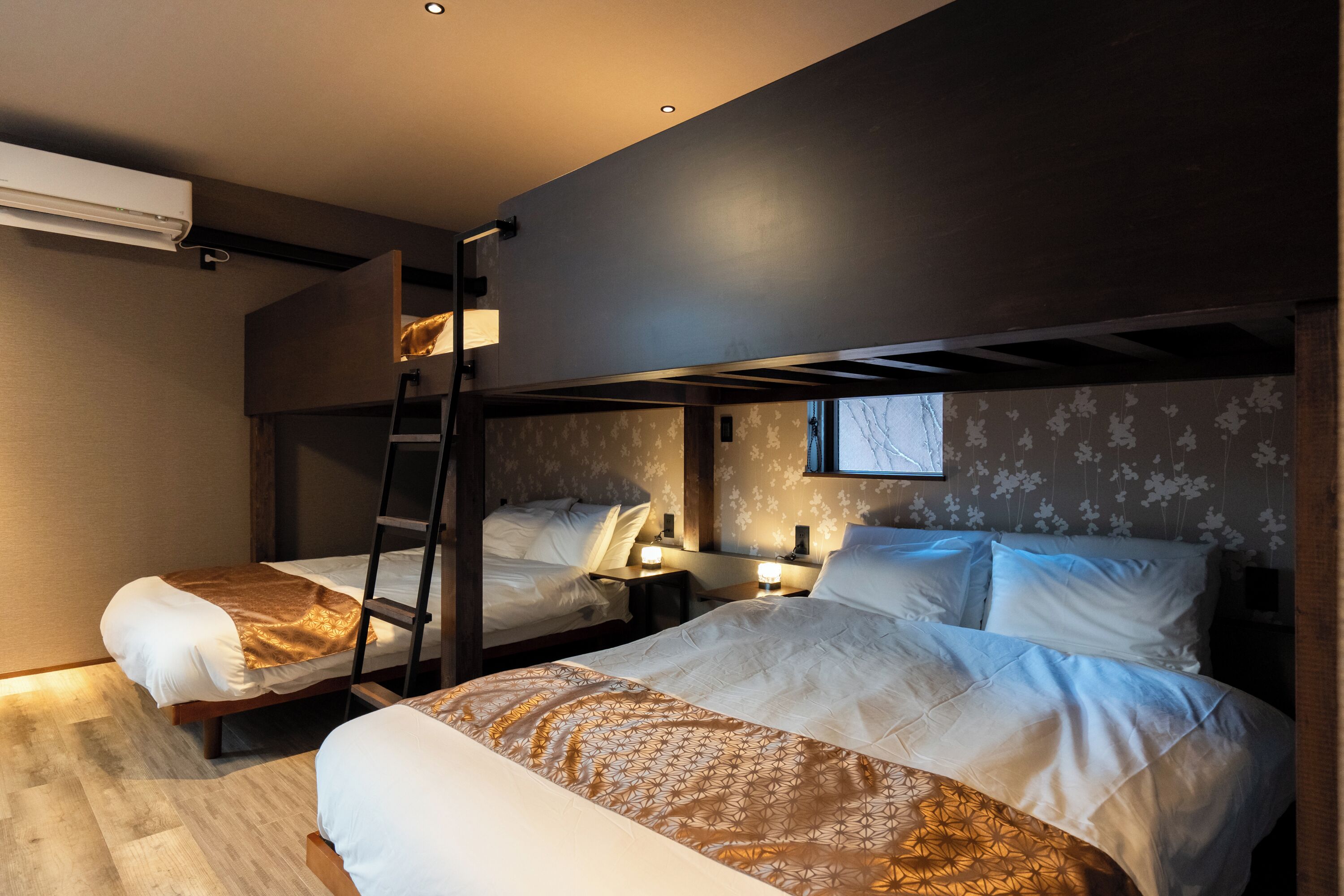 A room with two beds, a ladder, a window, and a wall-mounted air conditioner.
