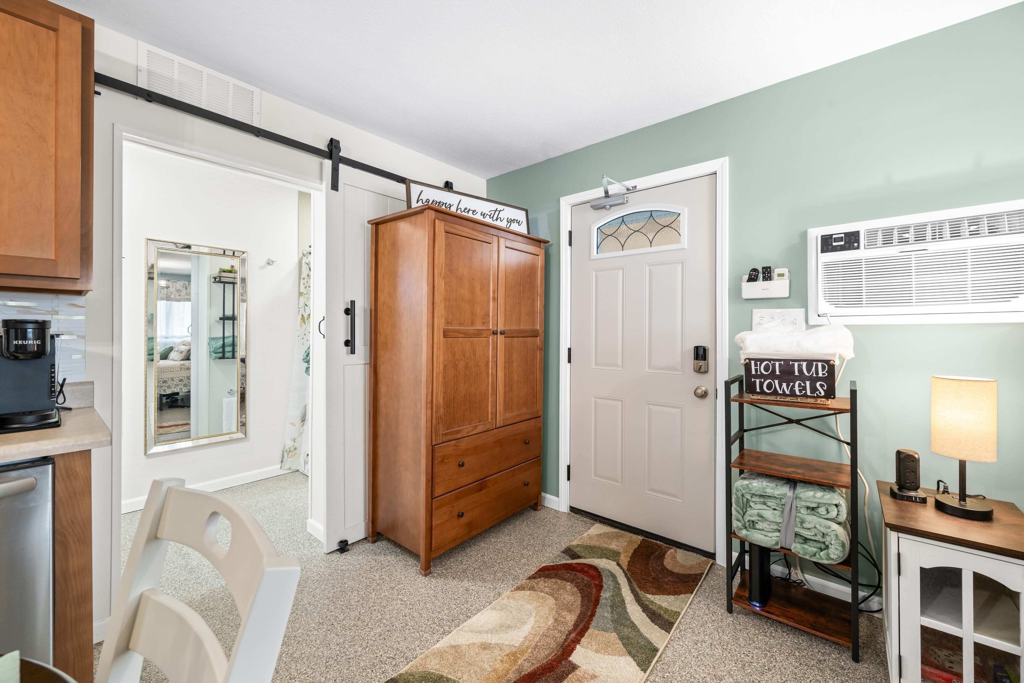 Una habitación con un armario de madera, una puerta corredera, un soporte para toallas de hidromasaje y una pequeña mesa con lámpara.