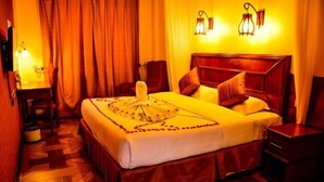 Une chambre d’hôtel avec un grand lit, une tête de lit en bois, un bureau avec une chaise et deux lampes fixées au mur.