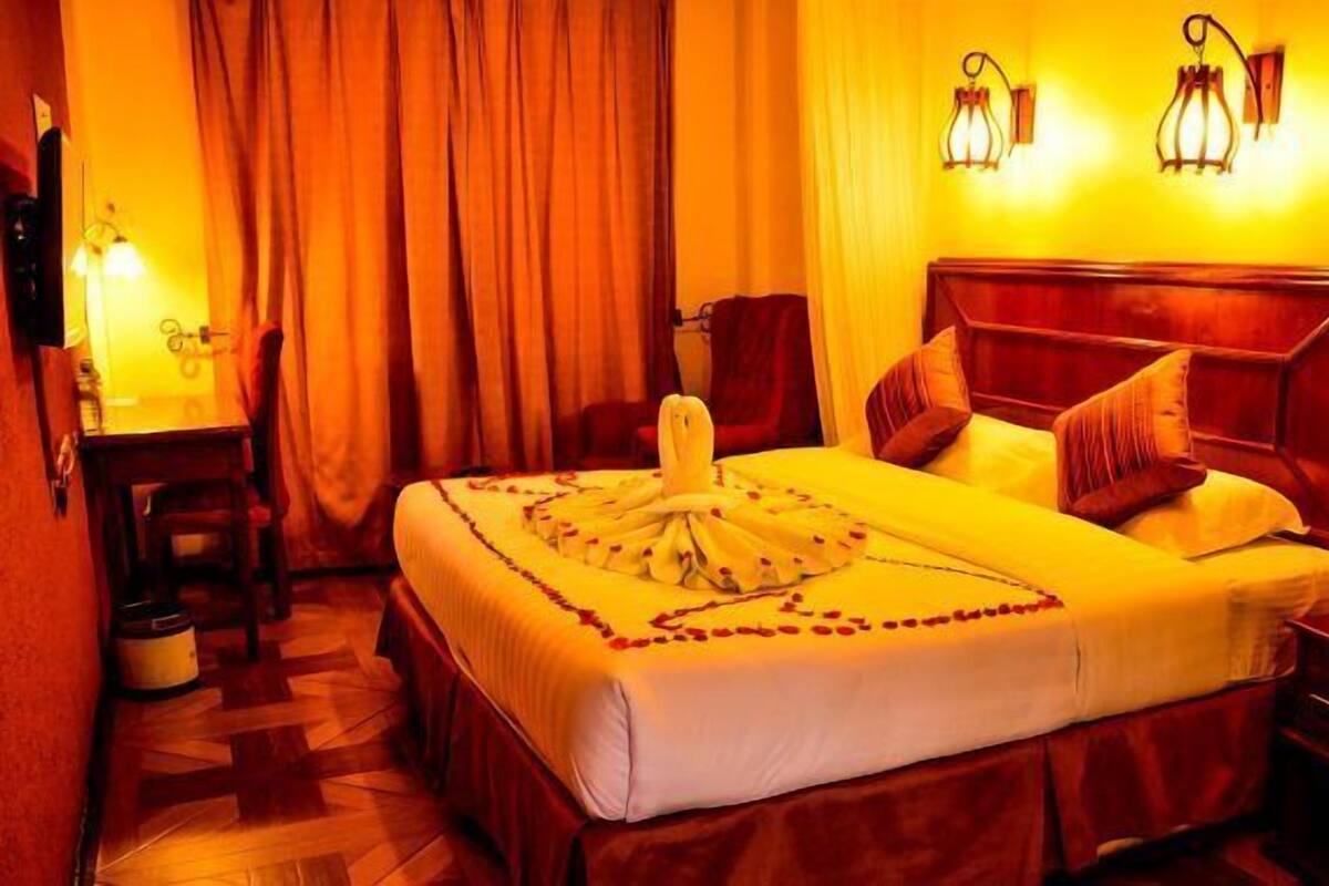 Ein Hotelzimmer mit einem großen Bett, einem hölzernen Kopfteil, einem Schreibtisch mit Stuhl und zwei Wandleuchten.