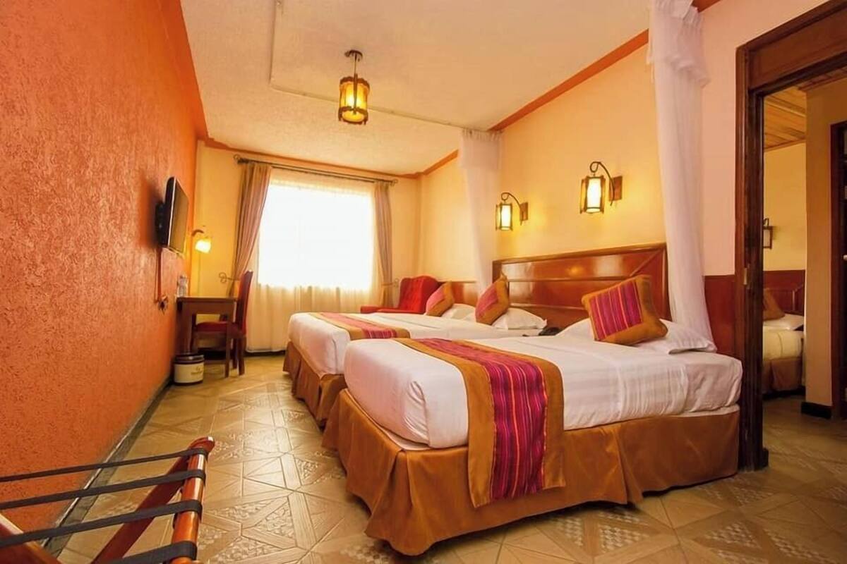 Ein Hotelzimmer mit zwei Betten, einem Fernseher und einem Fenster mit Vorhängen.