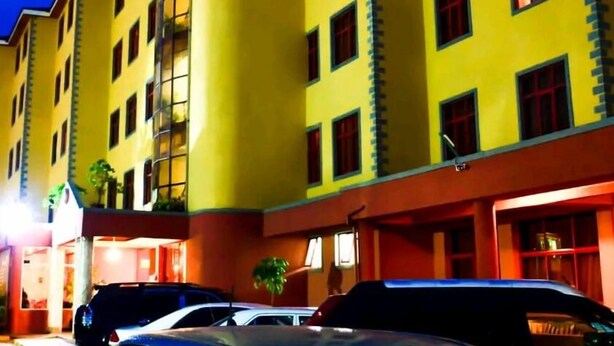 Un hôtel à plusieurs étages, doté d’une façade jaune, de nombreuses fenêtres et d’une entrée bien visible, avec des voitures garées devant.