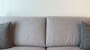 Olohuoneessa on harmaa sohva ja kaksi tummaa puuhyllyä. Ylemmällä hyllyllä on koriste-esineitä, kuten kannu, pieni kasvi ja kyltti, jossa lukee: ”TERVETULOA”. Alempi hylly sisältää puisen numeron ’88’, pienen kulhon ja koriste-esineen.