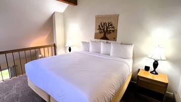 A neatly made bed with white linens, a nightstand with a lamp, and a wall-mounted artwork of a tree.