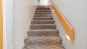 Una escalera con peldaños alfombrados y barandilla de madera, que conduce a un espacio interior.