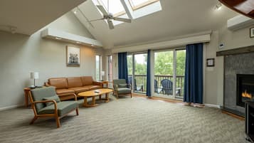 A spacious living room with a high ceiling, a fireplace, and a large sliding glass door leading to an outdoor deck.