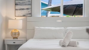 A hotel room with a bed, a bedside lamp, a wall-mounted artwork, and a window with an umbrella view.