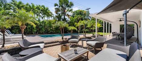 Relax by the pool surrounded by lush greenery and palm trees, with comfortable seating and a shaded area.