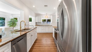 A modern kitchen with white cabinets, a stainless steel refrigerator, and a wooden countertop.
