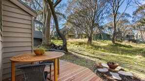 Une terrasse en bois avec une table et des chaises, entourée d’arbres et d’une pelouse.