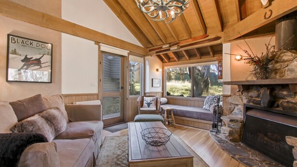 Un salon chaleureux avec une cheminée en pierre, un canapé, une table basse et une grande fenêtre donnant sur un jardin.