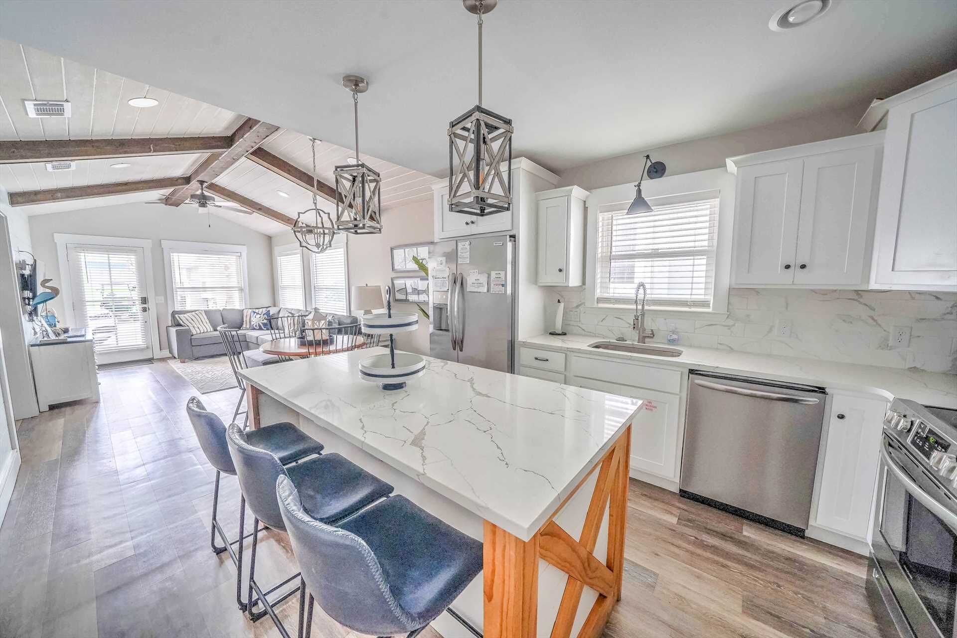 A modern kitchen with white cabinets, a marble island, and a stainless steel refrigerator.