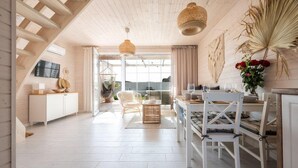 Una habitación amplia con techo alto, zona de comedor con mobiliario blanco y un gran ventanal que proporciona luz natural.