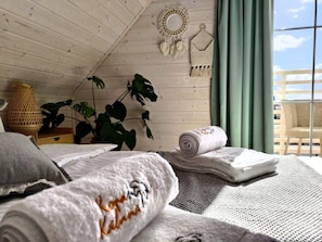 Una habitación acogedora con techo inclinado, una planta grande, una cama con toallas enrolladas y vistas a través de una ventana.