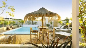 Un área de piscina con sillas de descanso, un parasol de paja y una pequeña mesa.