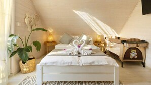 Un dormitorio acogedor y bien iluminado con techo de madera, una cama cuidadosamente hecha con toallas con forma de corazón, una lámpara de noche y un osito de peluche en una mesita de noche.