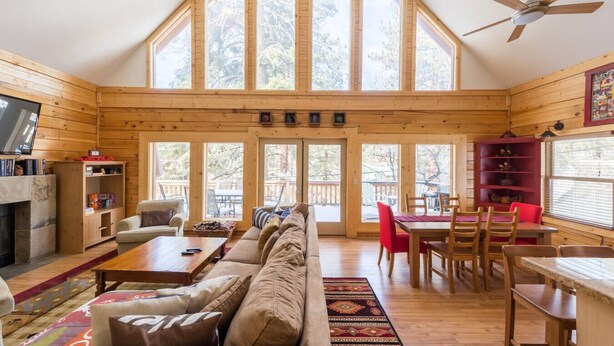 Une cabine spacieuse avec un plafond haut, de grandes fenêtres, un coin salon confortable avec un canapé et une table basse, une table à manger avec des chaises et une cheminée.