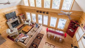 Une cabine spacieuse avec un plafond haut, des murs en bois, une cheminée, un téléviseur, un canapé, une table à manger et de grandes fenêtres.