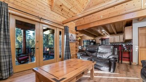 A wooden cabin interior with a large sliding glass door leading to an outdoor deck, a leather sofa, and a wooden table. - Indulge in the Perfect Family Adventure (Sugarloaf)