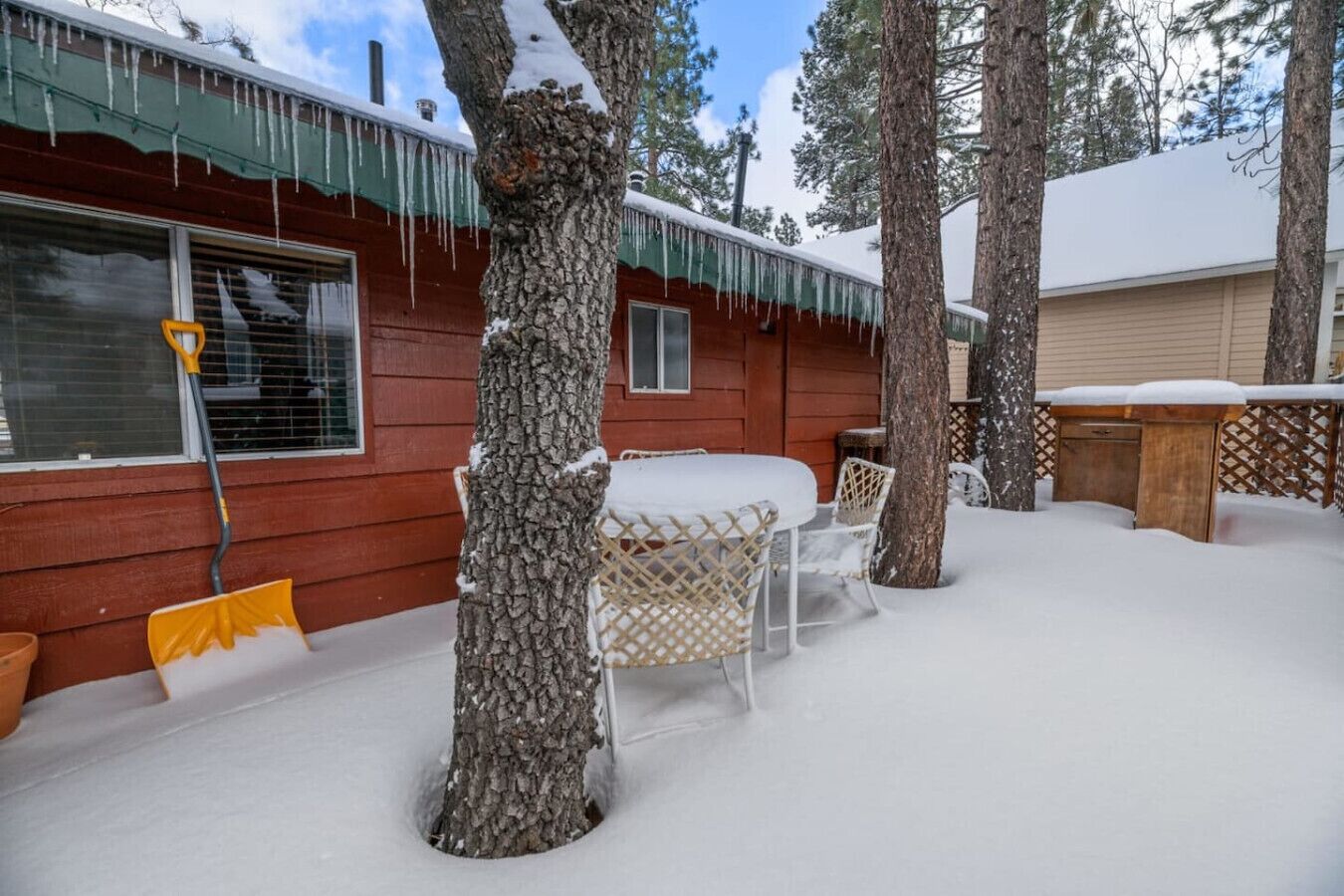 Eine Holzhütte mit einem mit Schnee bedeckten Deck und Gartenmöbeln.